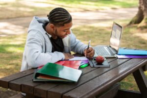 Black summer school student finishing Grade 12 math, happy teen outdoors, clear sunny path, light school supplies, academic freedom