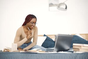 Young teenage girl sitting on her bed studying and using a lapto